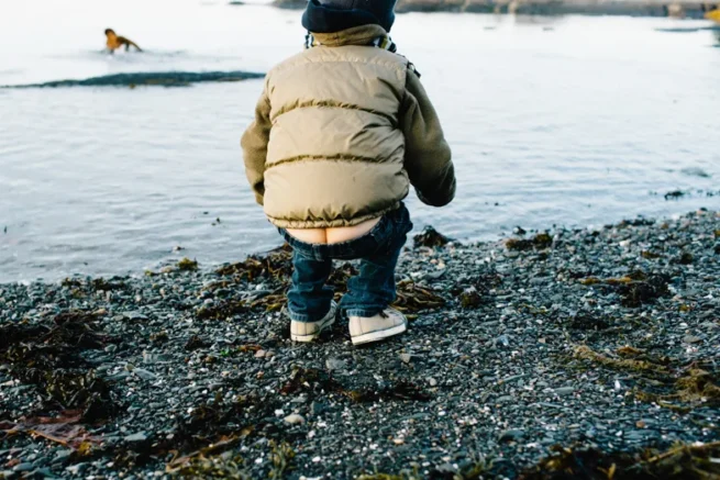Petit garçon de dos contemplant le Fleuve Saint-Laurent près des rochers à Rimouski, photographie couleur en haute résolution