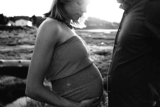 Couple attendant un enfant au coucher de soleil, portrait de grossesse en noir et blanc à Rimouski