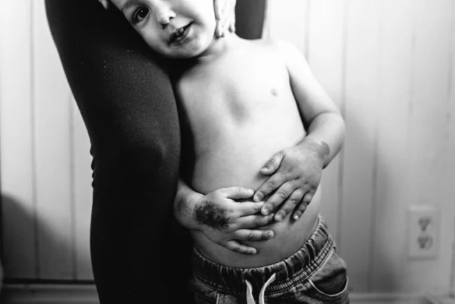 "Photographie en noir et blanc d'un jeune enfant souriant lors d'une séance photo en famille. Cette image capturée avec un style intemporel met en valeur la joie et l'innocence de l'enfant, idéale pour des souvenirs familiaux précieux."