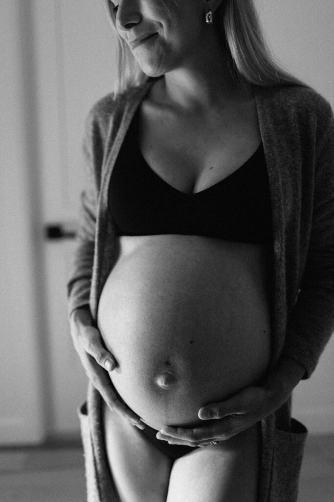 Plan rapproché en noir et blanc d'une femme enceinte se tenant le ventre, illustrant l'approche humaine et la confiance cultivée par 5Mphotographie, votre photographe maternité à Rimouski.