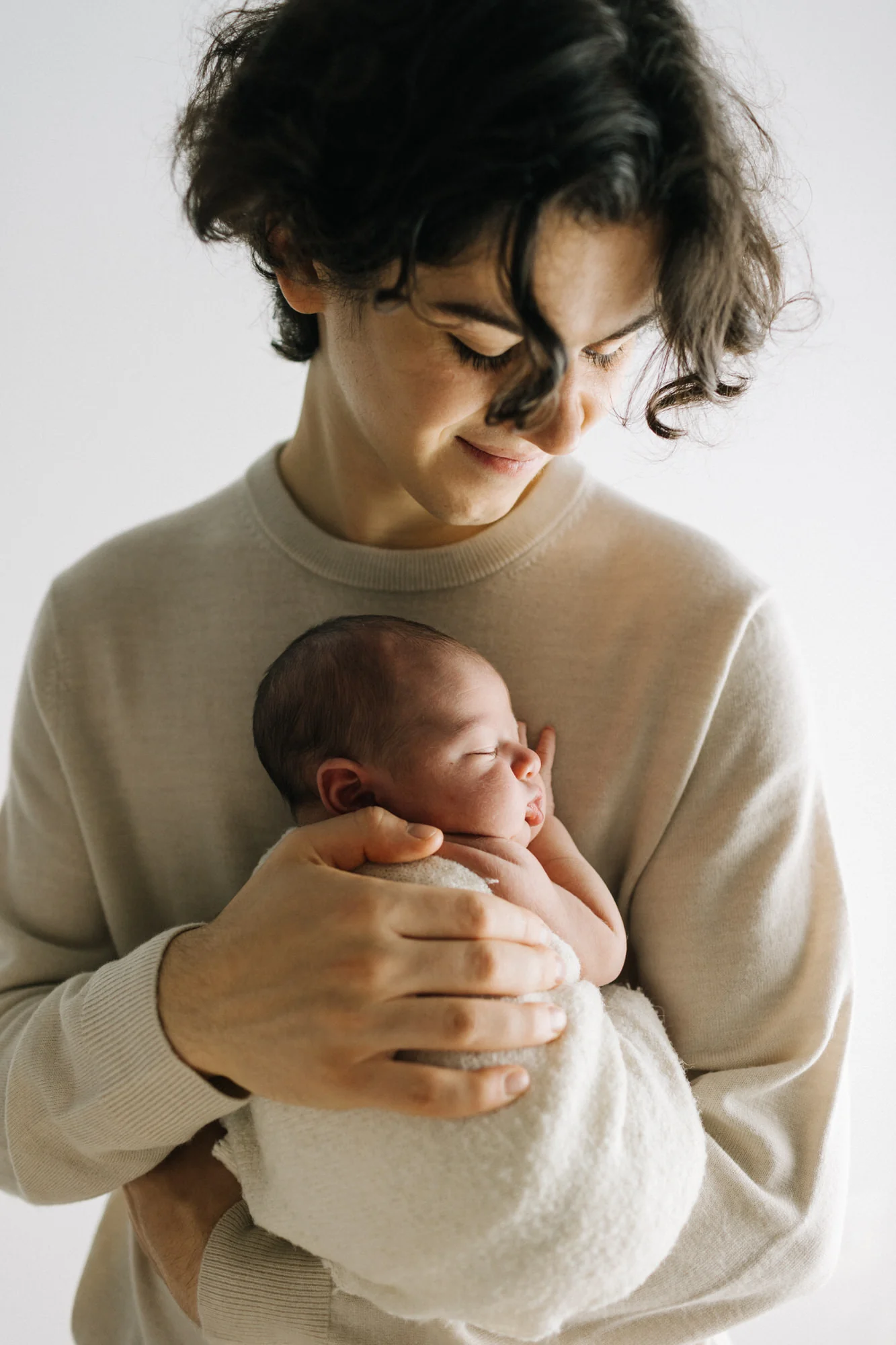 Un papa serre tendrement son nouveau-né contre elle, illustrant la douceur et l'aura de la naissance lors d'une séance photo à Rimouski.