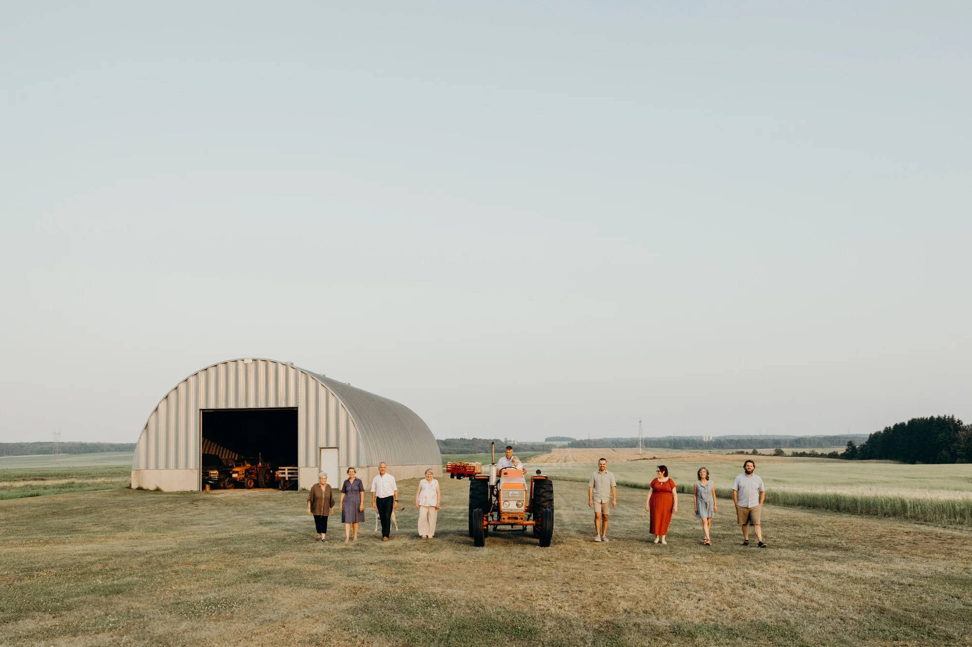 Photo de famille multigénérationnelle devant une grange ancestrale et un vieux tracteur à St-Pascal.
