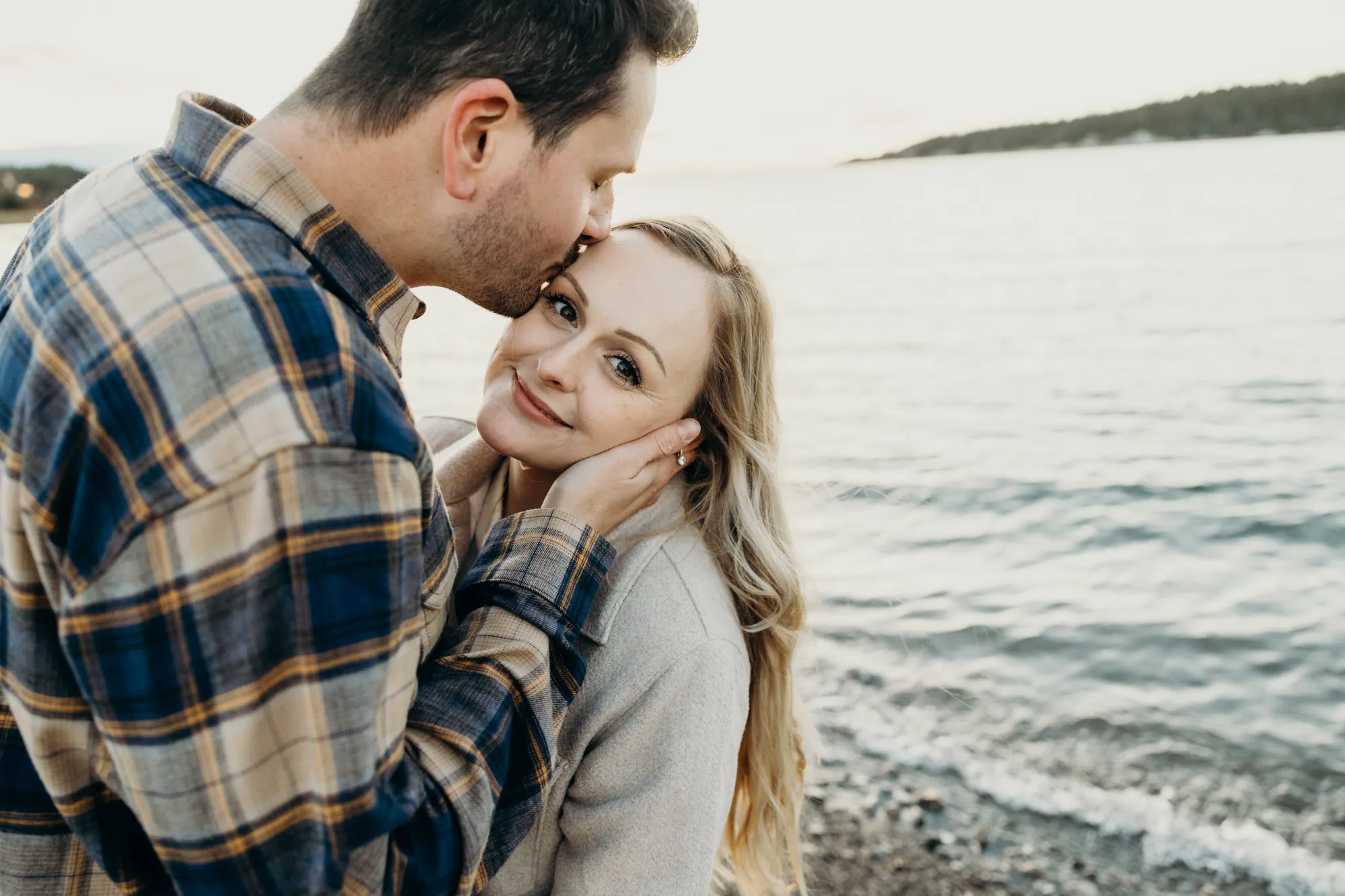 Baiser sur le front au bord du fleuve sous une lumière de fin de journée.