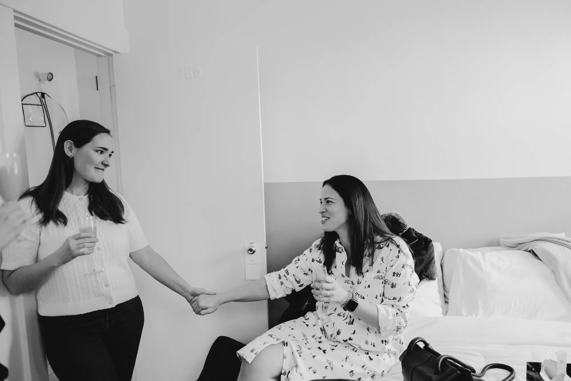 La mariée assise sur son lit de préparation, tenant la main d'une amie.