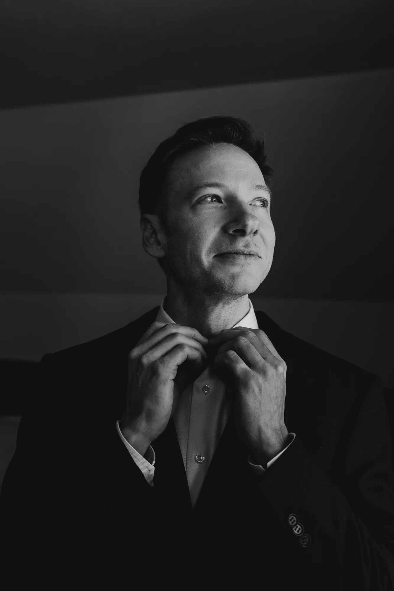 Gros plan en noir et blanc du marié ajustant son nœud papillon devant un miroir.