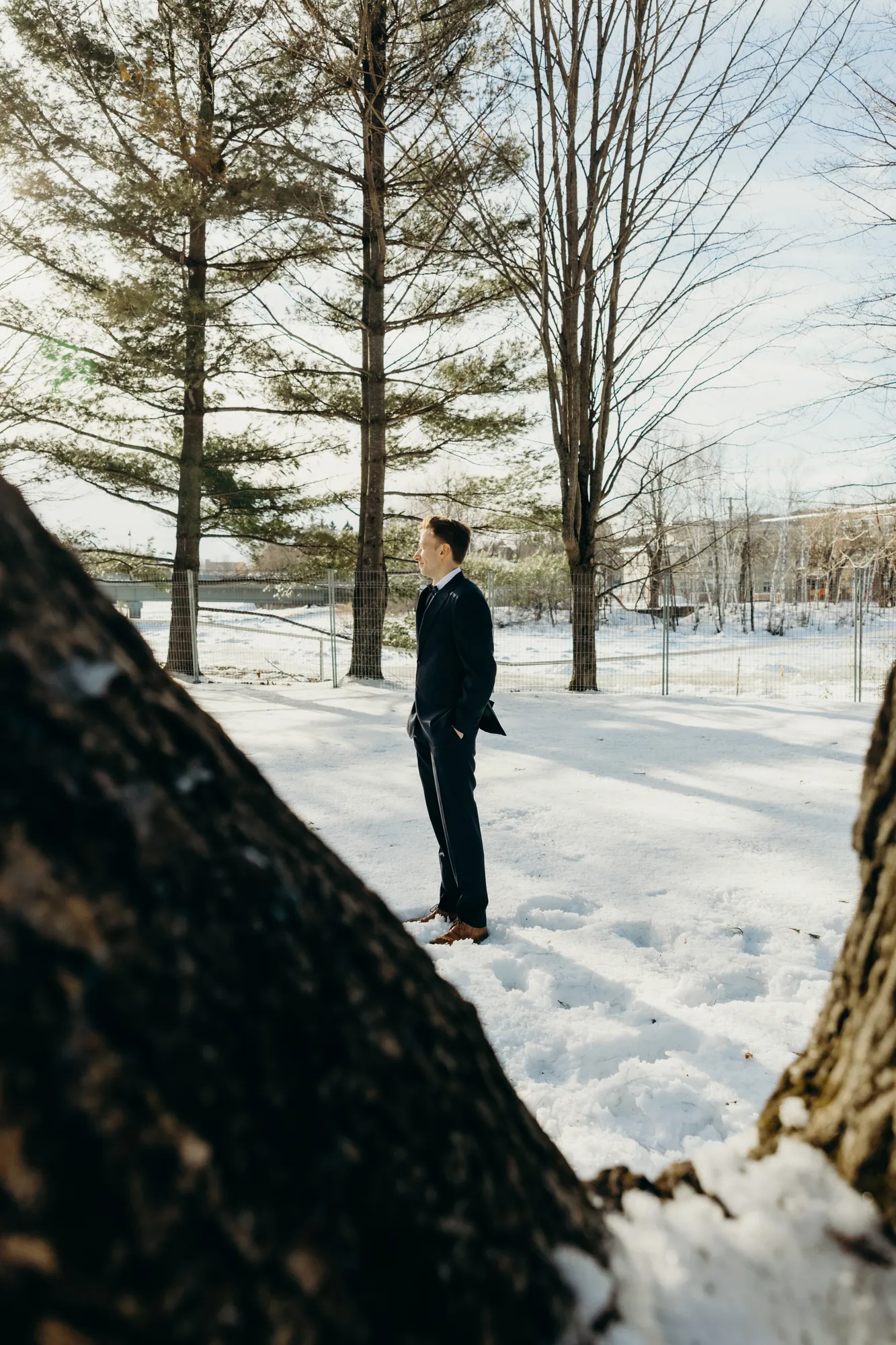 Portrait du marié seul en forêt d'hiver, mettant en valeur son costume sombre sur fond blanc.