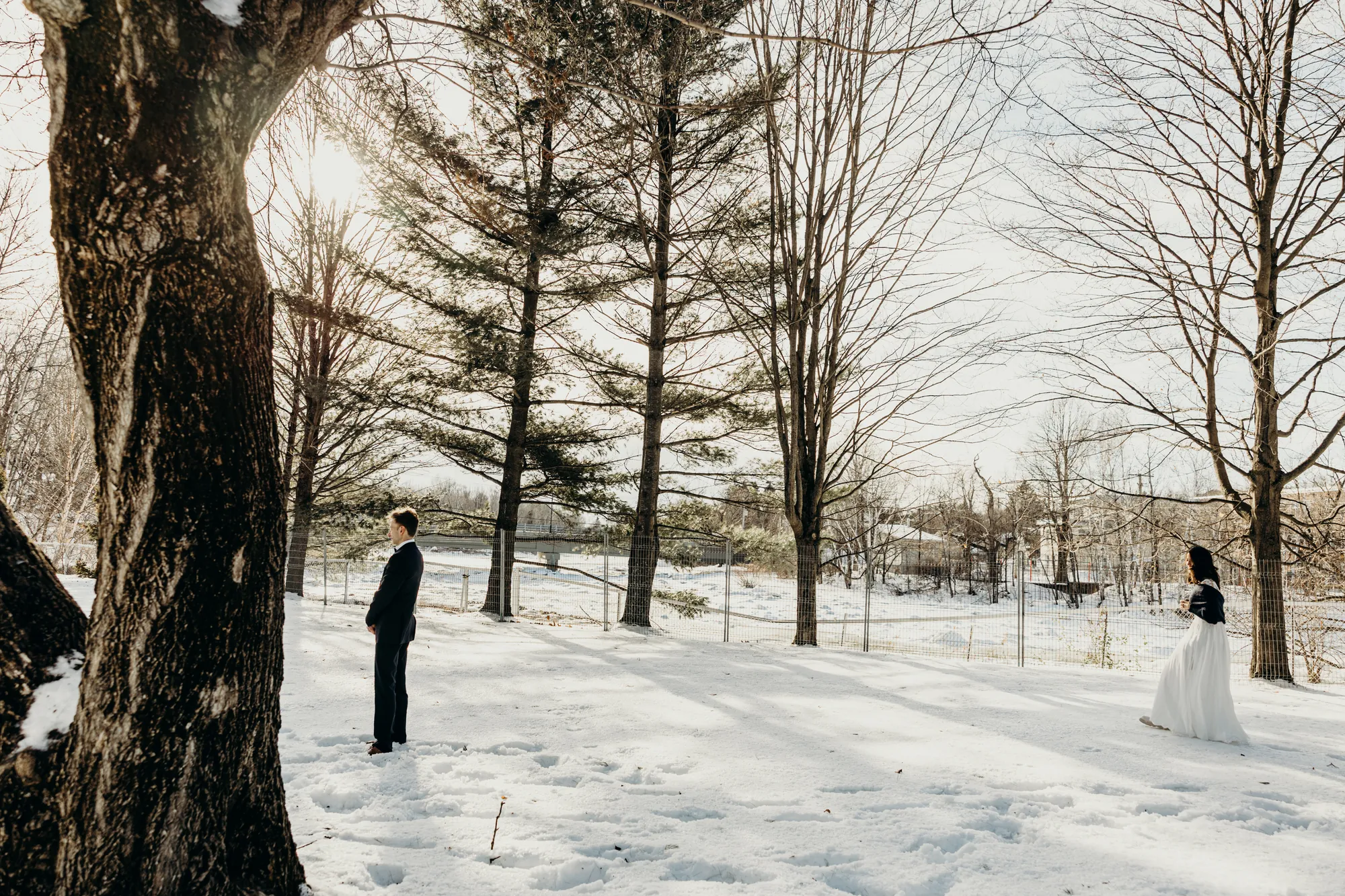 Le marié Julien debout près d'un grand arbre noir contrastant avec la neige blanche.