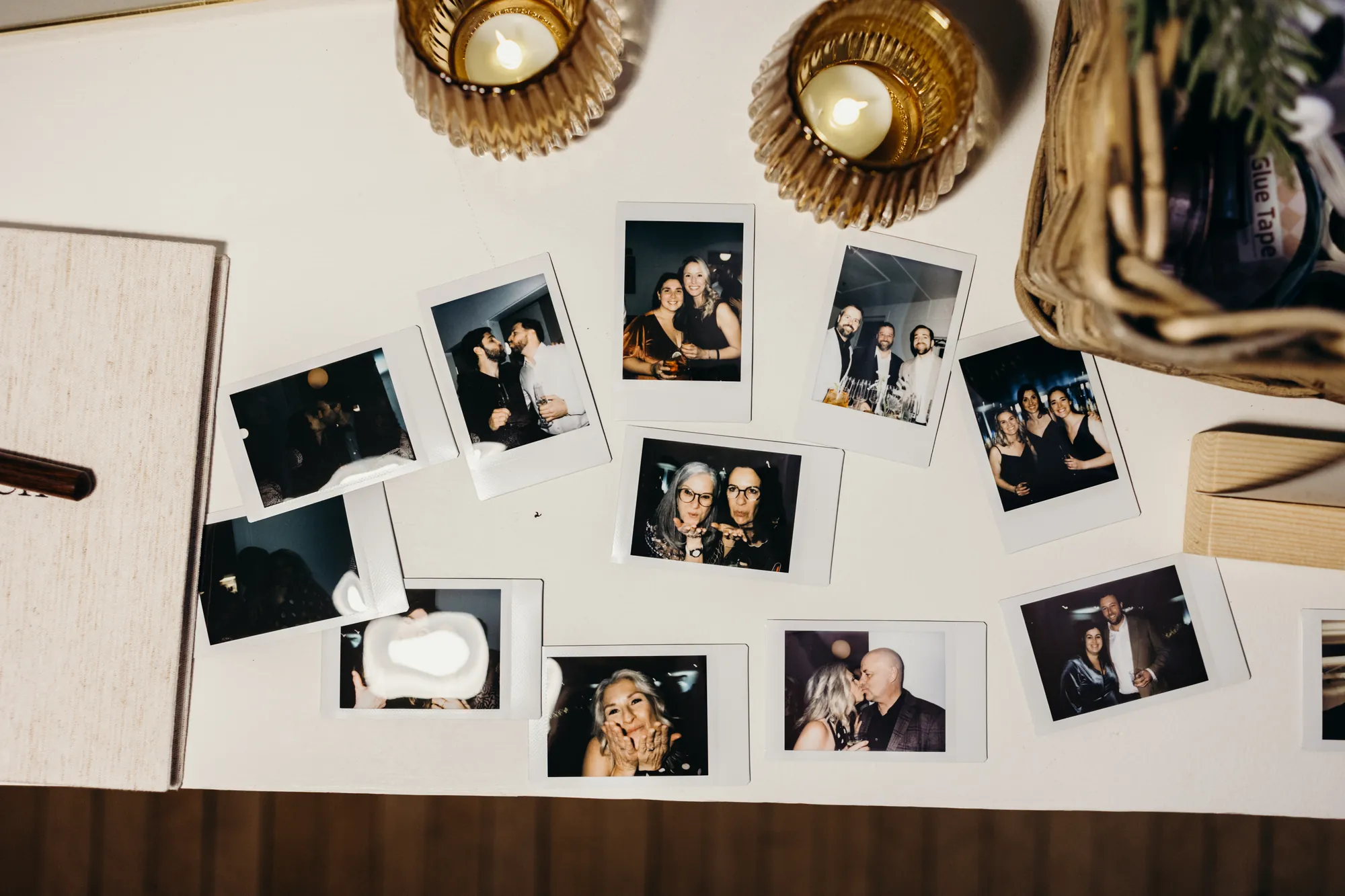 Composition de photos polaroid d'invités épinglées sur un mur blanc avec photophores dorés.