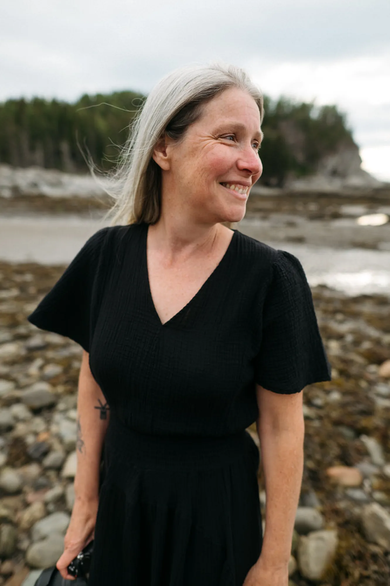 Catherine Hudon-photographe de Rimouski qui pose dans une robe noir avec le parc du bic en arrière plan.
