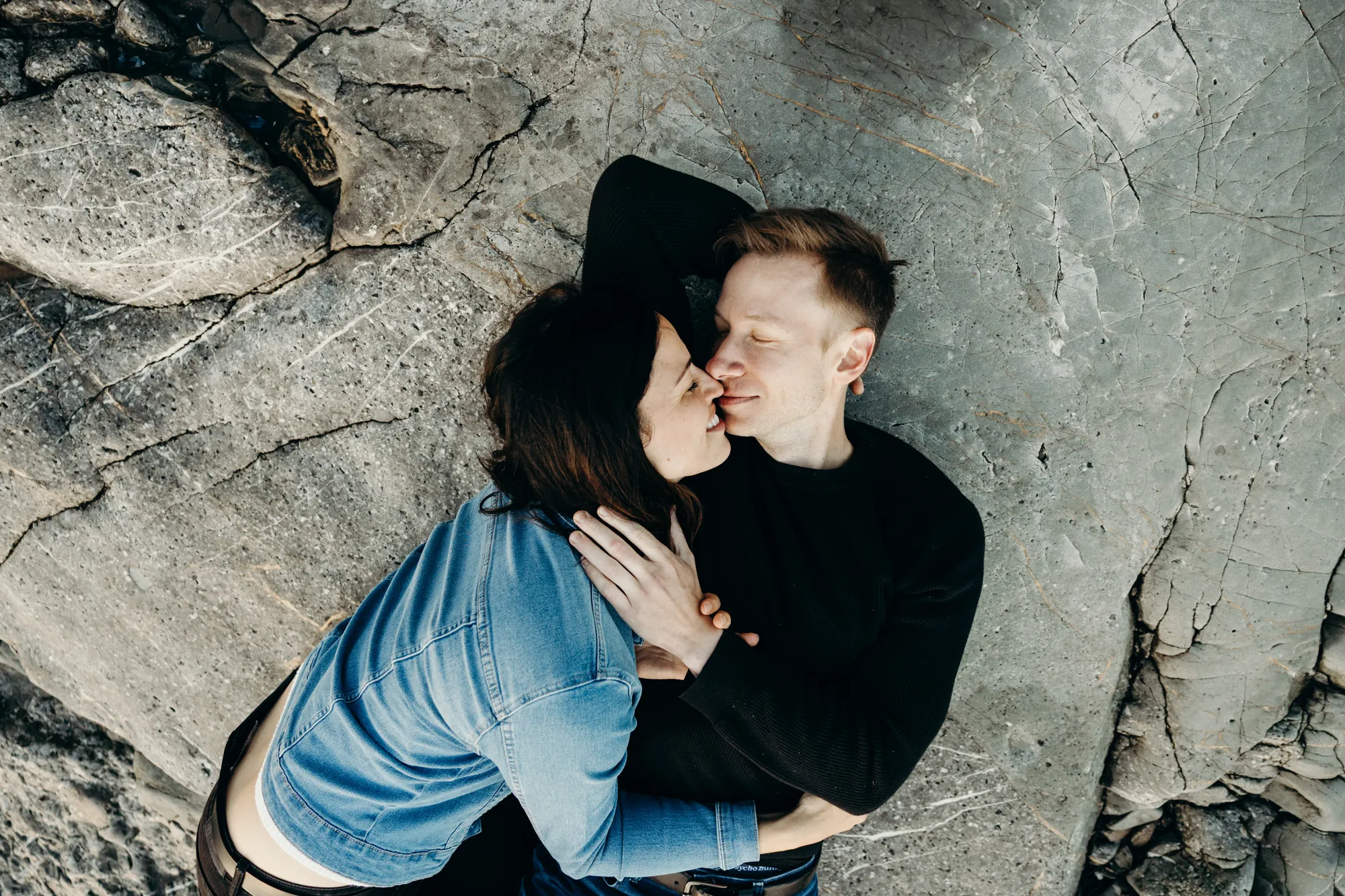 Vue en plongée d'un couple allongé sur les rochers du littoral.