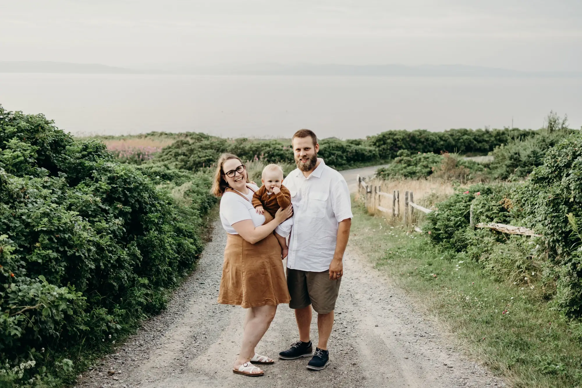 Couple avec enfant dans leur bras dans un chemin qui mène au fleuve st laurent qui pose pour 5Mphotographie.
