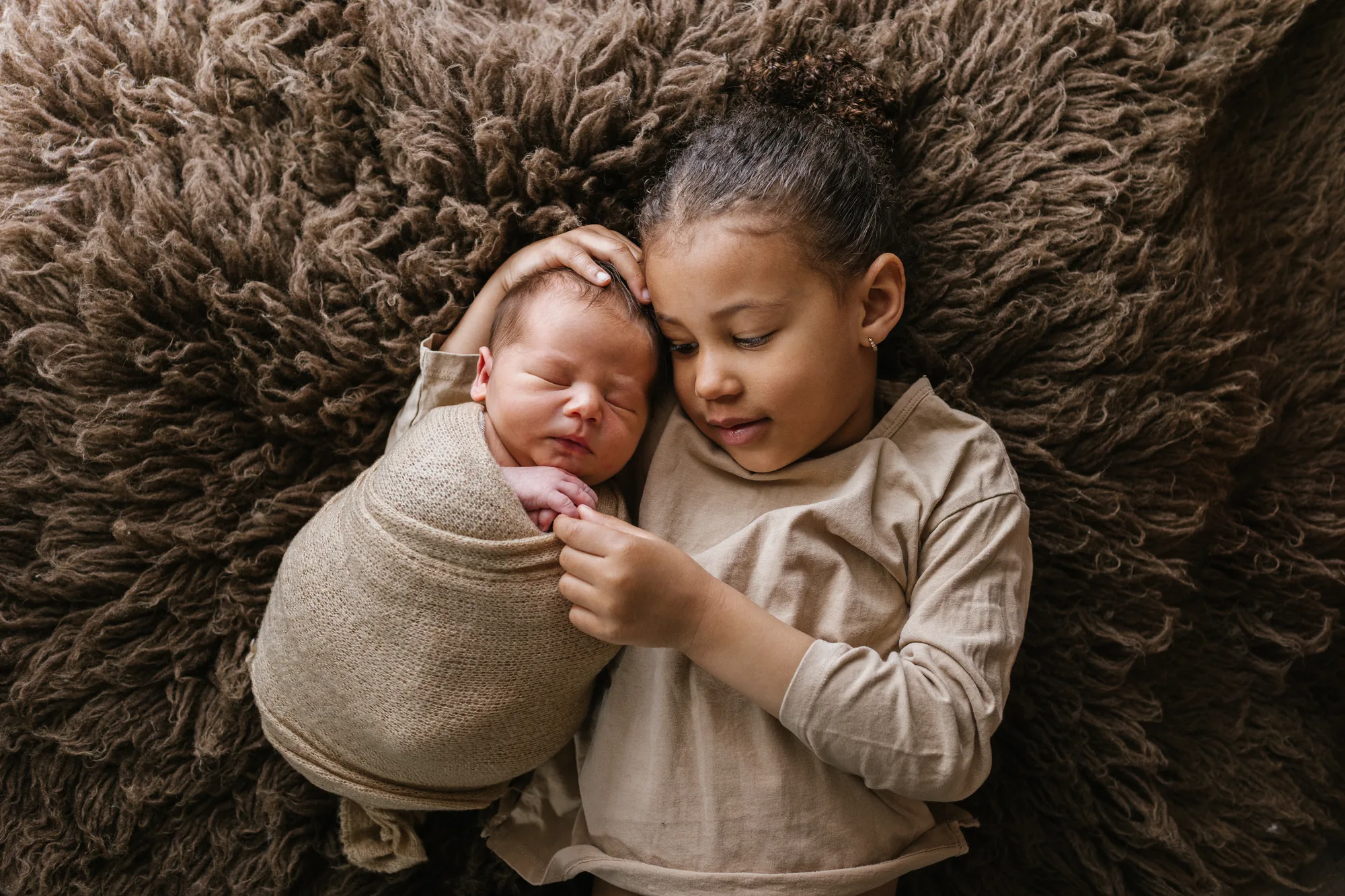 Abrielle veillant sur son frère nouveau-né emmailloté, une séance famille douce. 