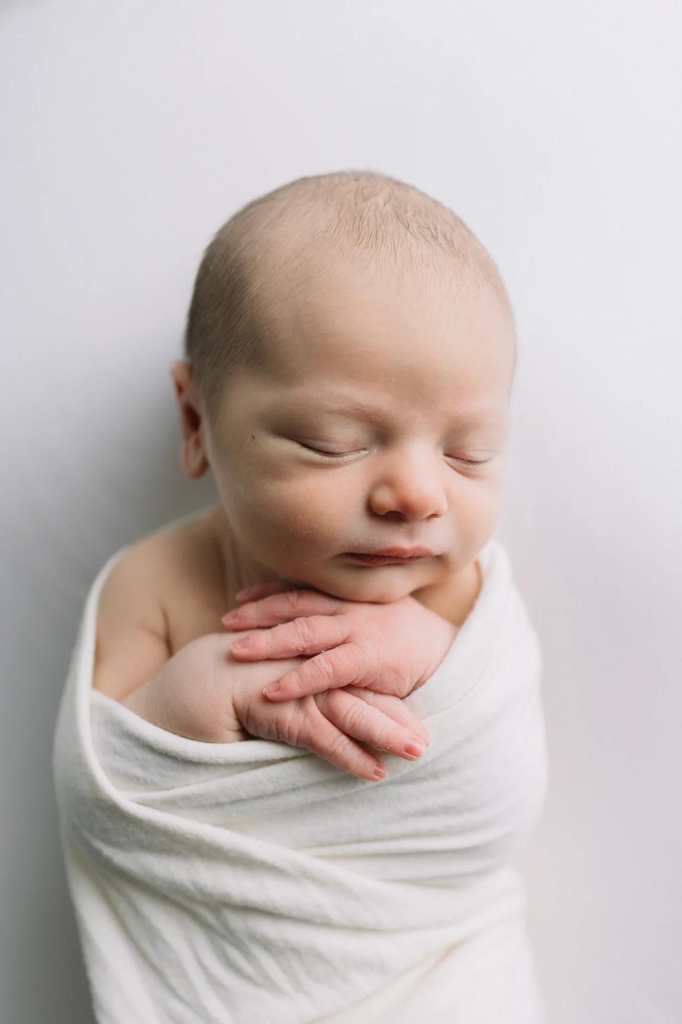 Nouveau-né Noam emmailloté dans un tissu blanc pur, pose de studio réalisée à domicile