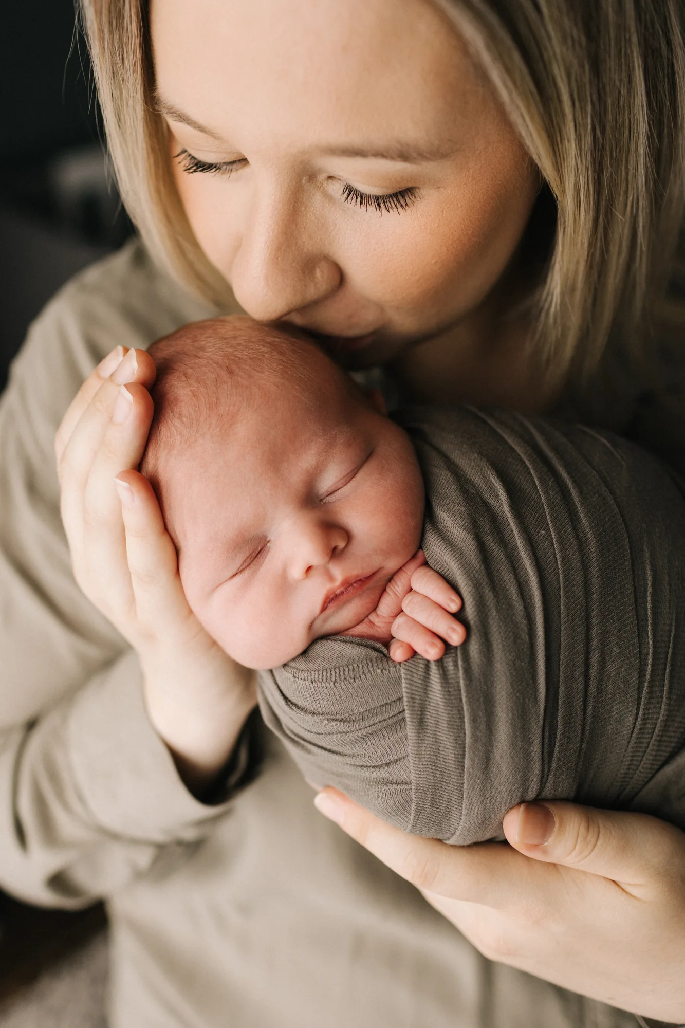 Séance photo nouveau-né à Rimouski : une maman embrasse son bébé Marc-Édouard emmailloté.