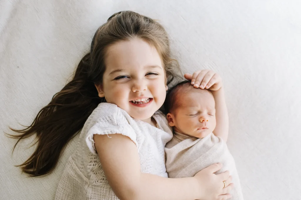 Claire serrant son frère Paul dans ses bras pour une séance photo nouveau-né.