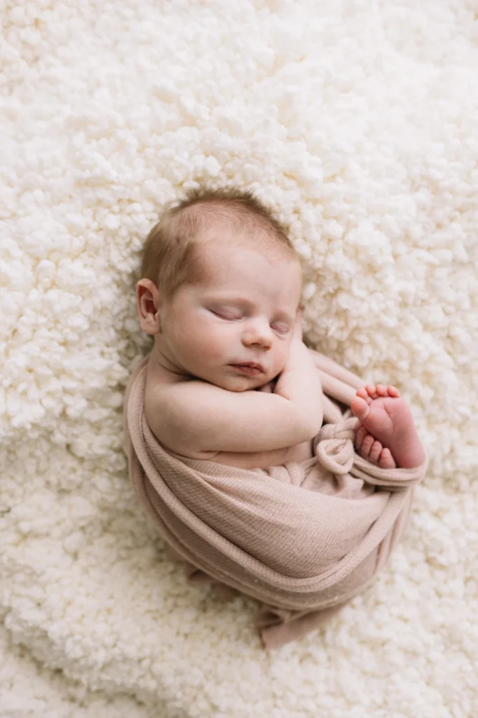 Bébé Annabelle emmailloté dans un cocon mauve sur un tapis de fourrure blanche.
