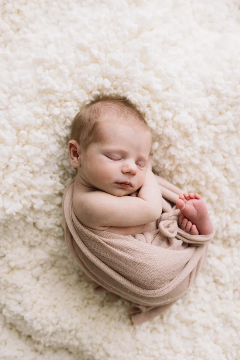 Bébé Annabelle emmailloté dans un cocon mauve sur un tapis de fourrure blanche.