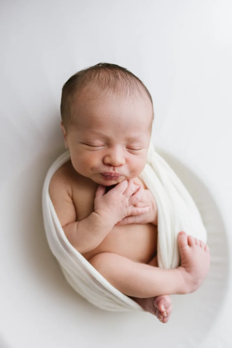 Isaac emmailloté dans un tissu blanc pur, mains sous le menton, studio Rimouski.