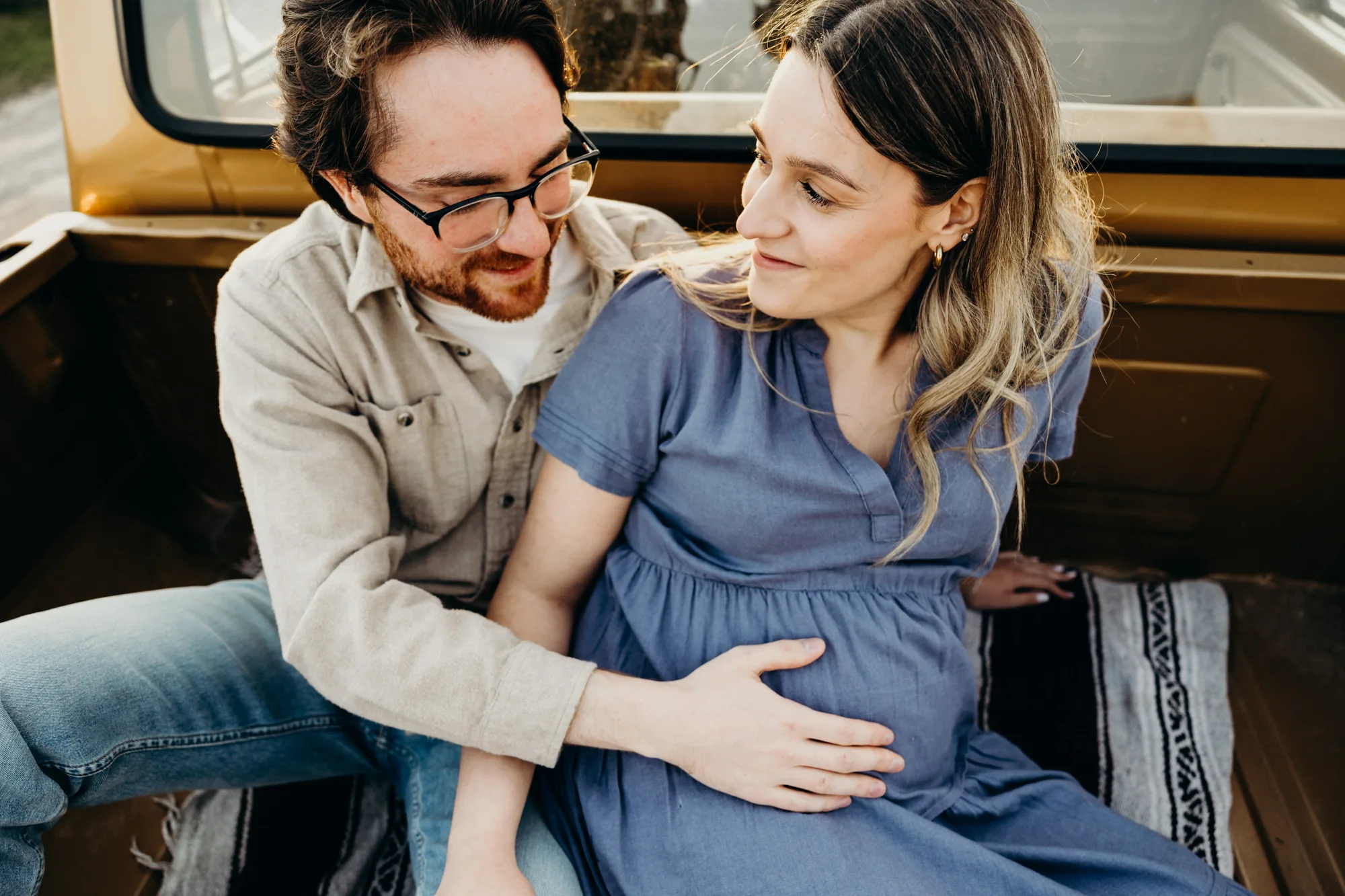 Homme qui touche le ventre de sa femme enceinte avec une robe bleu assis dans un pick-up
