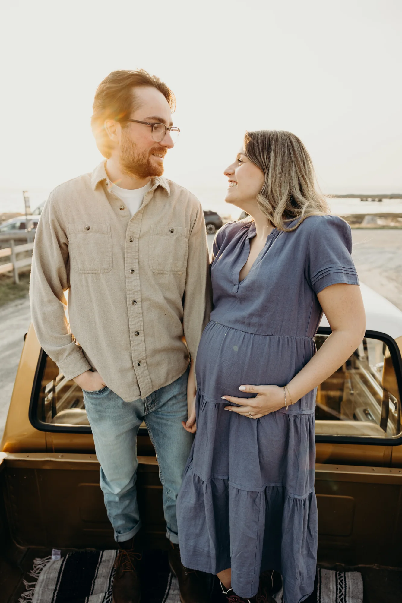 Couple homme et femme enceinte avec robe bleu qui tient son ventre se regarde avec amour.