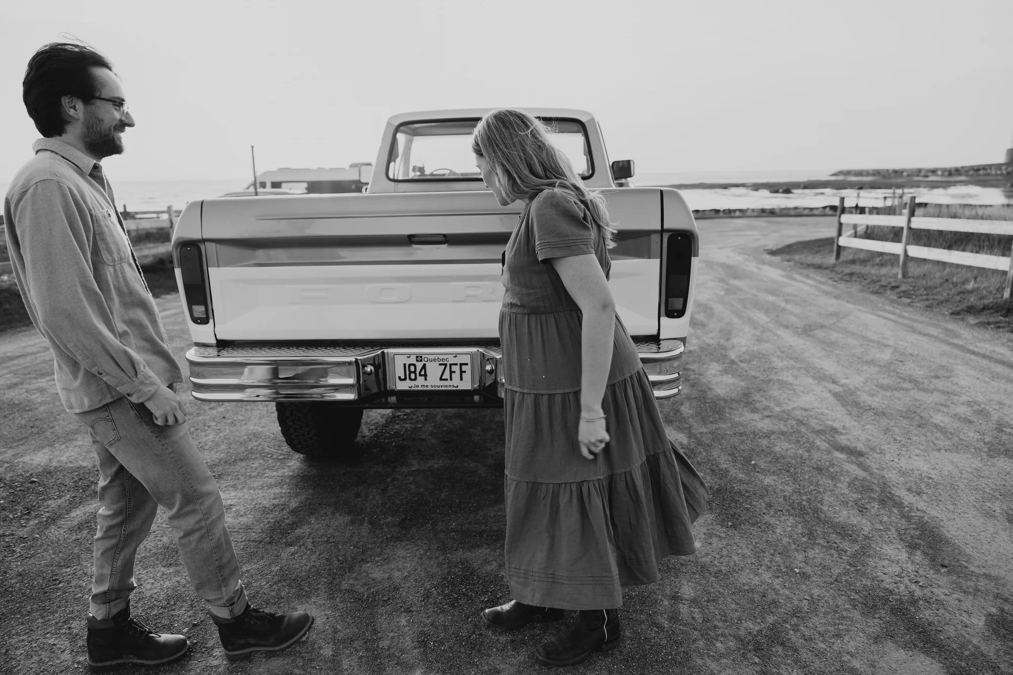 Couple en séance photo maternité en noir et blanc devant un vieux pick-up