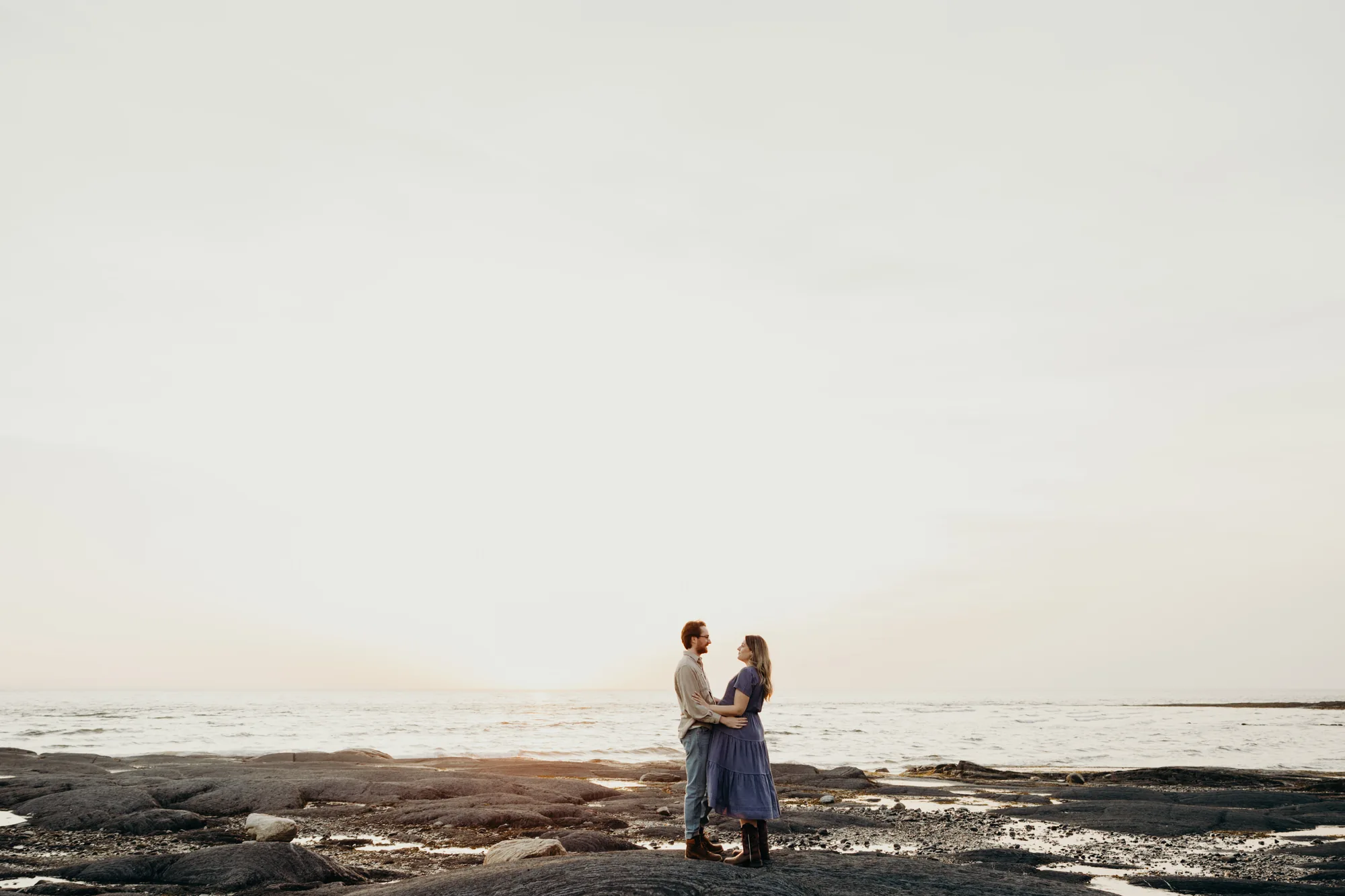 Couple devant le fleuve St-Laurent au coucher du soleil qui se regardent sous la lentille de la photographe de Rimouski.